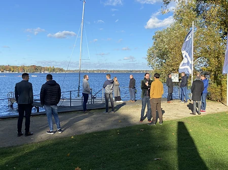 Gruppe von Personen am Seeufer mit Boot und Flagge